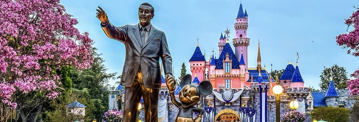 The Walt Disney and Mickey Mouse statue in front of Sleeping Beauty Castle, framed by pink blossoms.