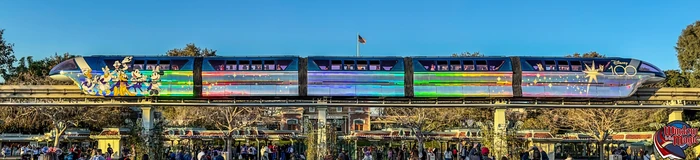 A colorful Disney100 monorail passes above the Disneyland entrance.